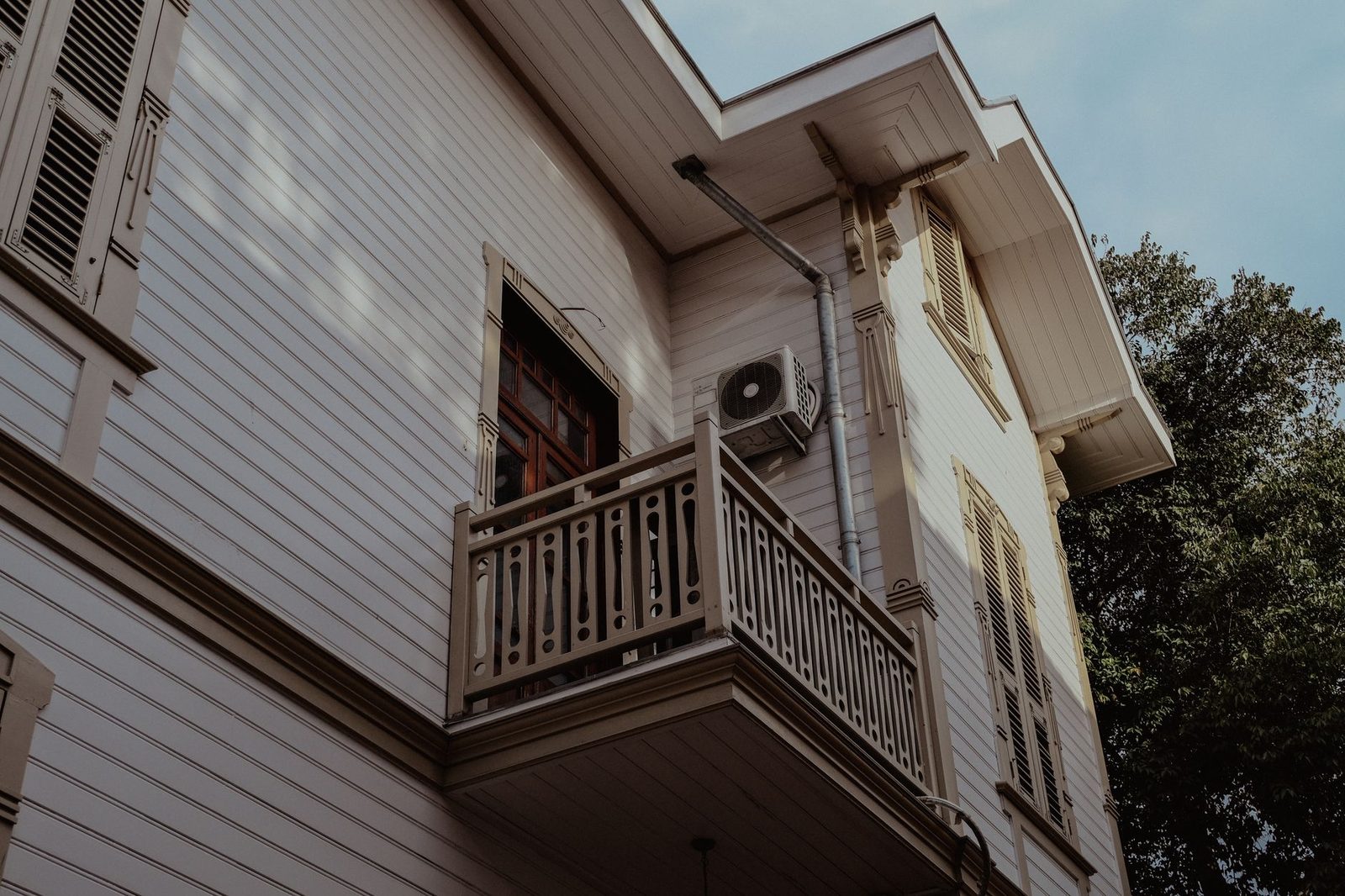 Unité extérieure de climatisation fixée sur la façade en bois d'une maison, près d'un balcon