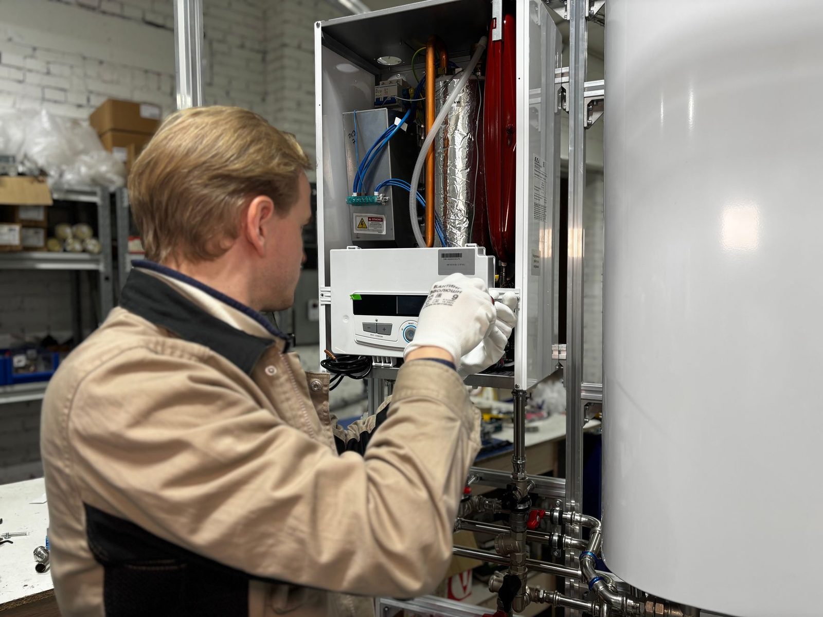 Technicien ganté intervenant sur le module intérieur ouvert d'une pompe à chaleur avec ballon d'eau