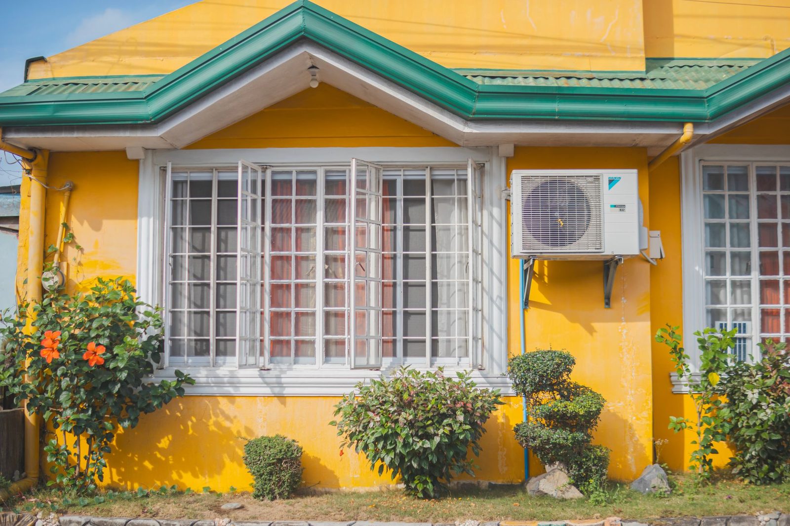 Unité extérieure de climatisation fixée sur la façade jaune d'une maison, près d'une fenêtre