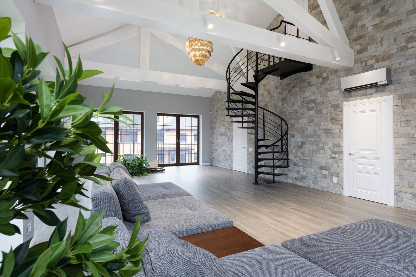 White wall-mounted air conditioner installed on a stone wall in a bright living room with a spiral staircase