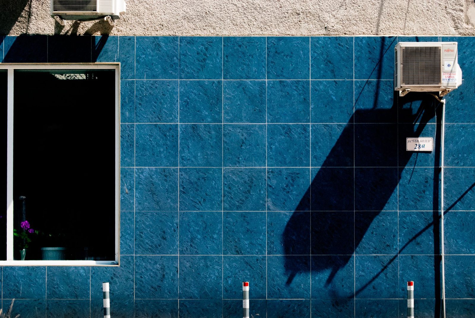Außeneinheiten von Klimaanlagen an einer blau geflieste Fassade neben einem Fenster