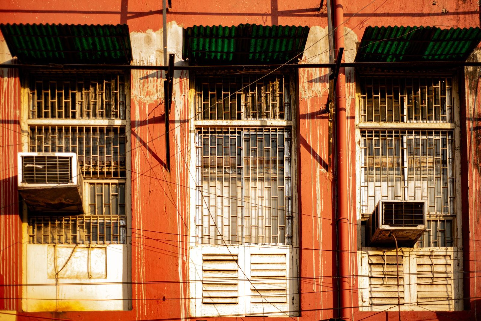 Condizionatori da finestra installati sulla facciata rossa di un edificio con finestre dotate di grate