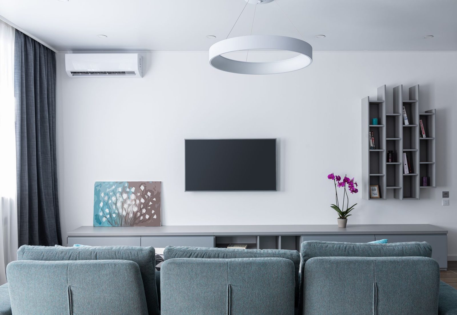 Climatizzatore a parete bianco installato in un salotto moderno con divano grigio, televisore e mensole