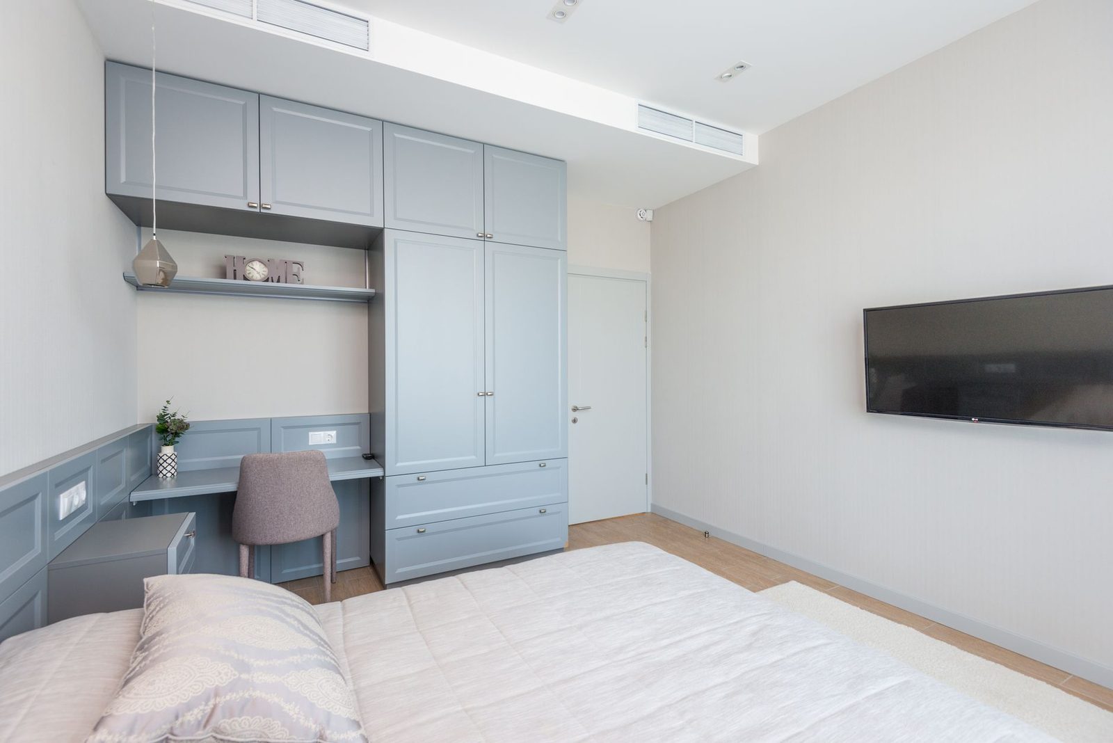 Camera da letto moderna con letto, armadi grigio-blu, televisore a parete e griglie di ventilazione a soffitto