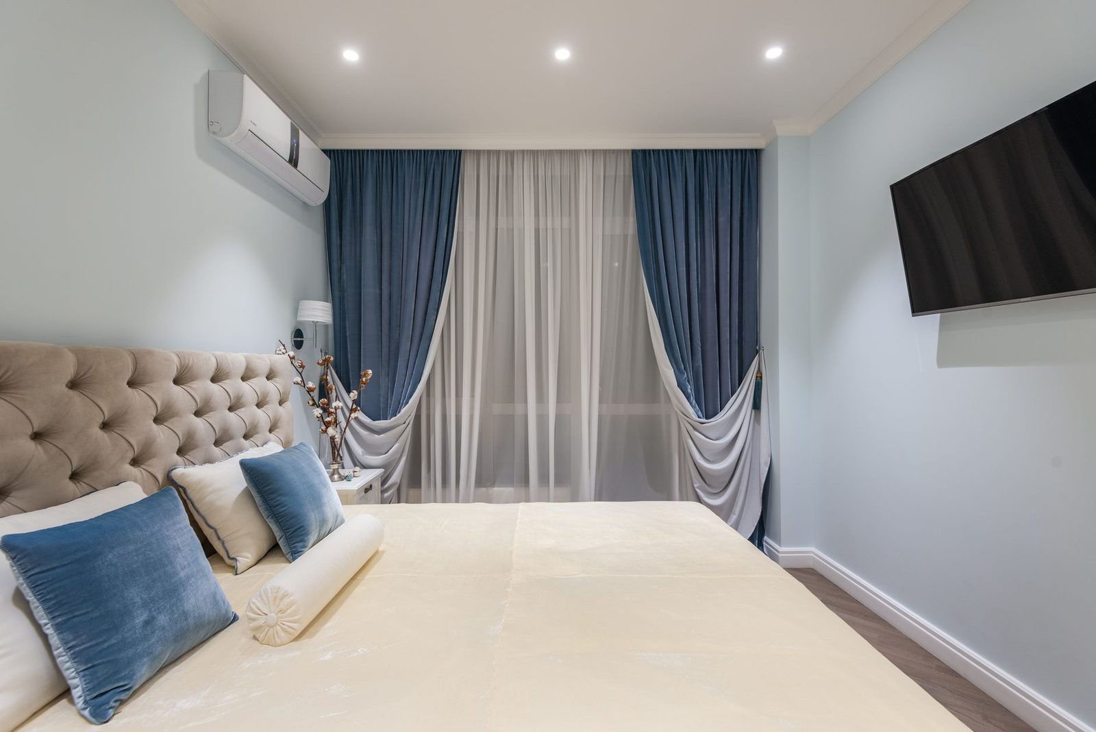 Aire acondicionado de pared blanco instalado en un dormitorio moderno con cortinas azules, cama y televisor