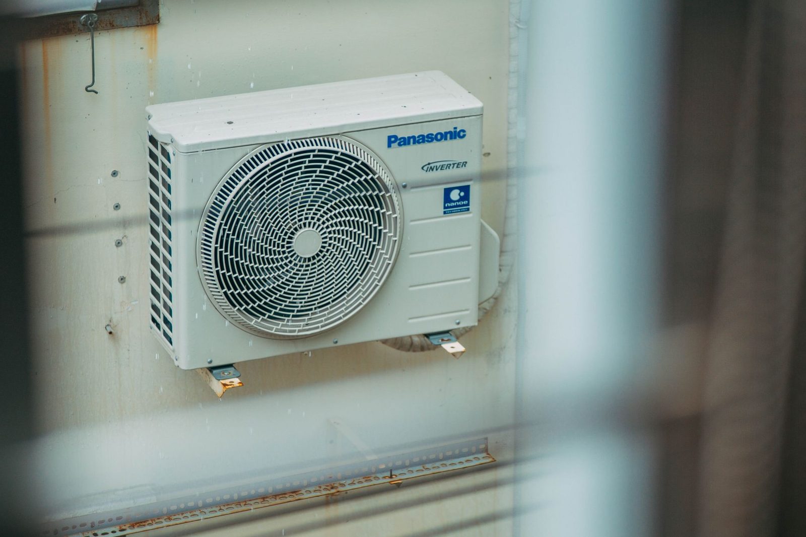 Unité extérieure de pompe à chaleur air-air Panasonic fixée sur un mur blanc.
